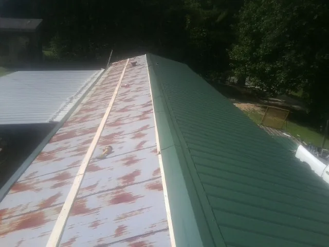 Old rusted panels beside newly installed green metal roofing — Wind Damage Roof Repair by Roofing Brothers in Pittsfield
