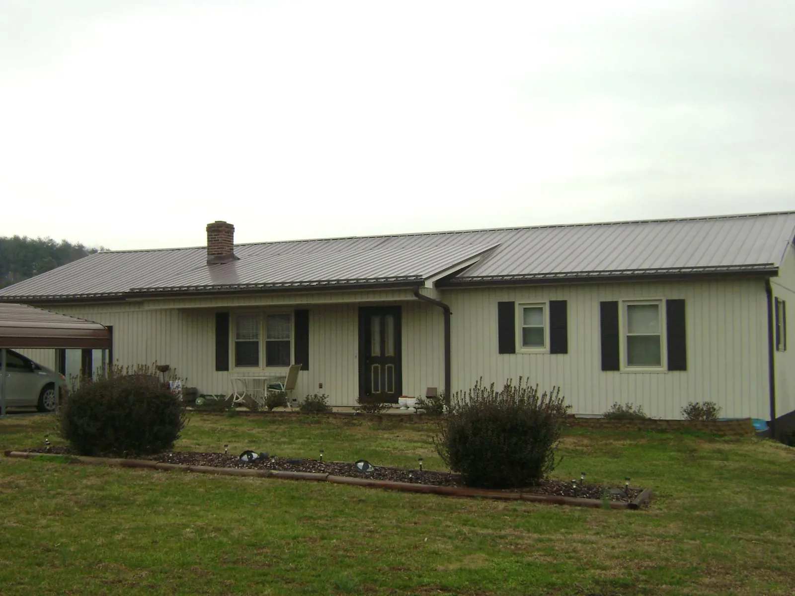 Brown metal roof on a cream sided ranch home with a brick chimney in Pittsfield
