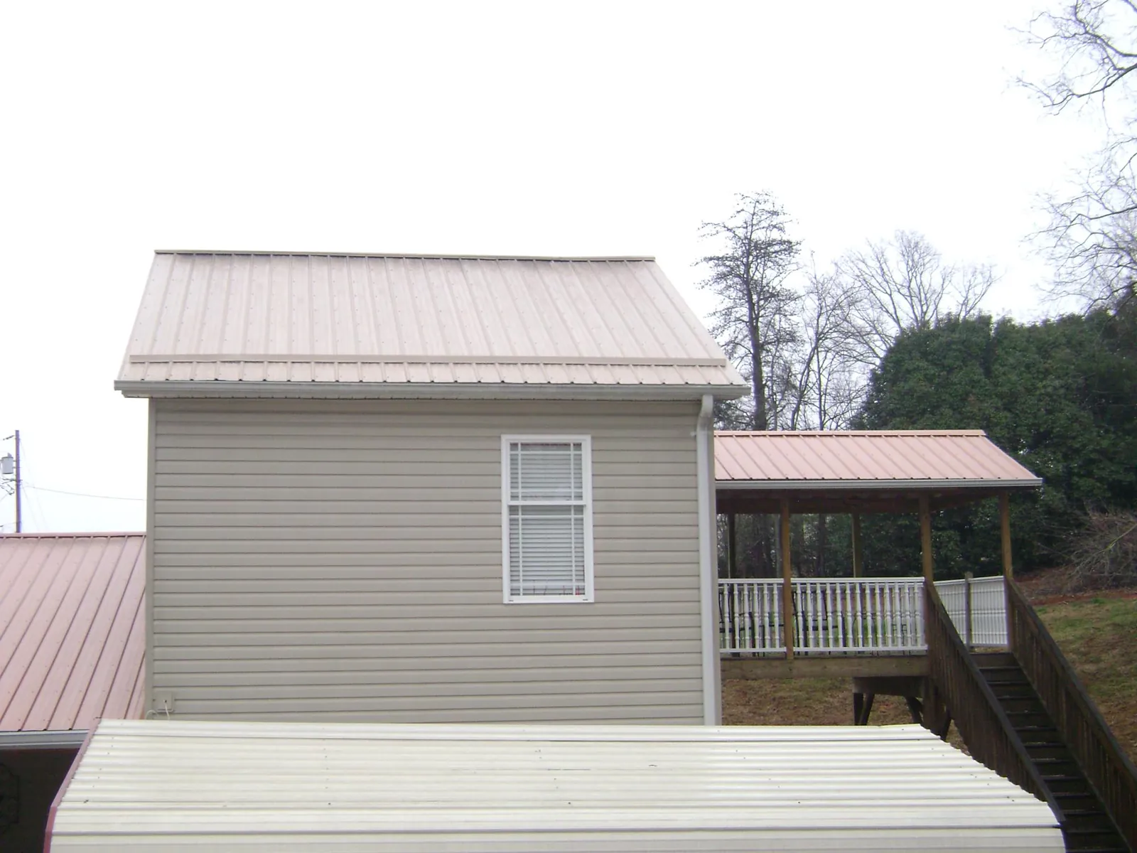 Tan metal roofs on a two story addition and attached porch, from a Roof Replacement job in Pittsfield